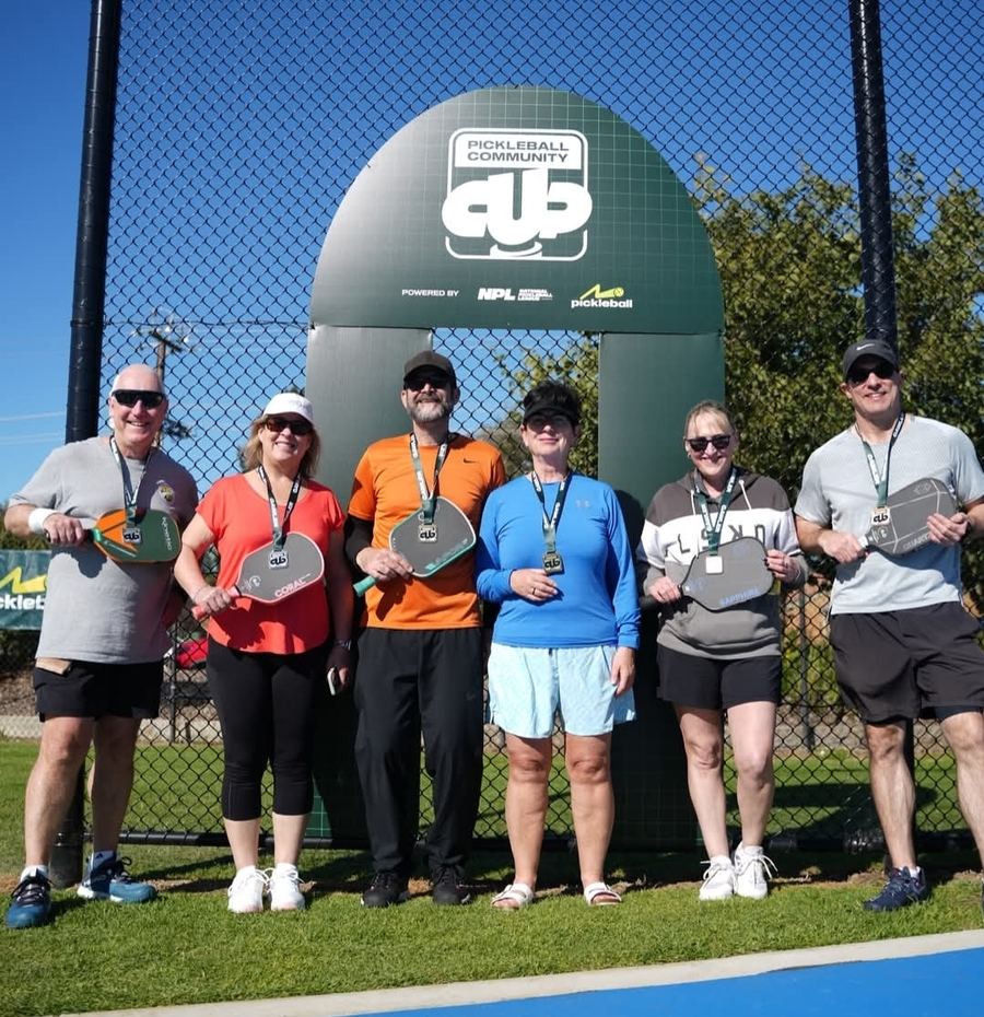 Six players with paddles posing after a Pickleball Community Cup tournament