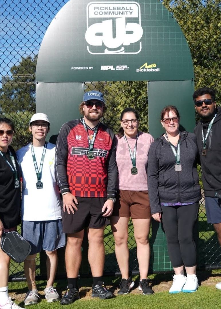 Six players with paddles posing after a Pickleball Community Cup tournament