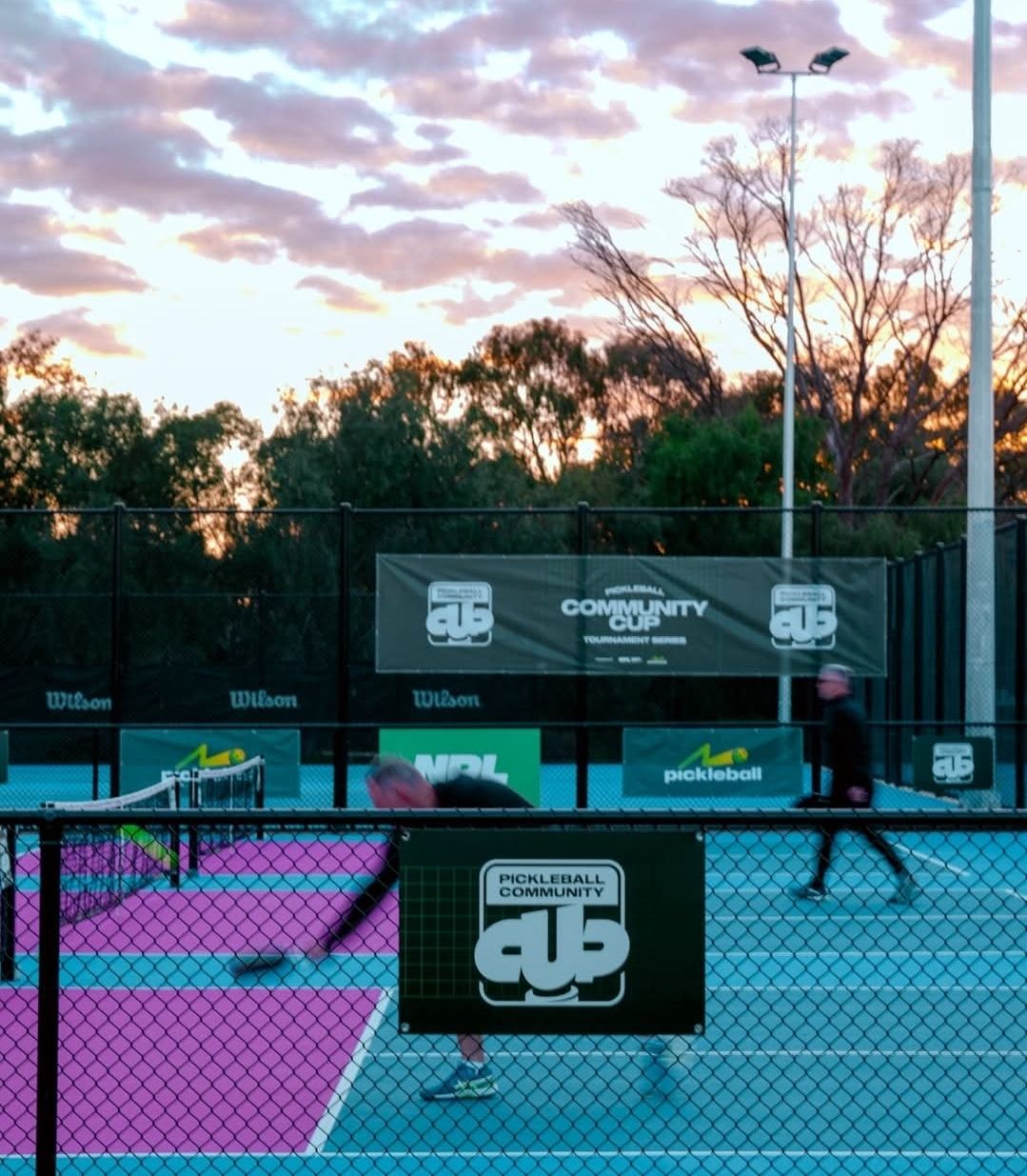 Dusk falling over the pickleball courts during a tournament, floodlights on